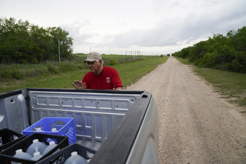 Migrant rights activist Eduardo Canales unloads jugs of water for a water drop Saturday, May 15, 2021, in Falfurrias, Texas. Every week, Canales fills up blue water drums that are spread throughout a vast valley of Texas ranchlands and brush. They are there for migrants who venture into the rough terrain to avoid being caught and sent back to Mexico. (AP Photo/Gregory Bull)