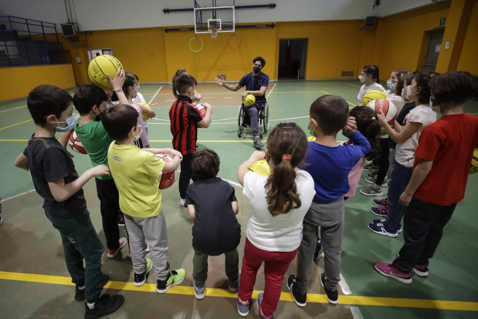 Adolfo Damian Berdun, of Argentina, a professional player and captain of the Argentine basketball Paralympic team, teaches children basketball at a primary school in Verano Brianza, outskirt of Milan, Italy, Tuesday, May 11, 2021. Four second-grade classes in the Milan suburb of Verano Brianza have been learning to play basketball this spring from a real pro. They also getting a lesson in diversity. Their basketball coach for the last month has been Adolfo Damian Berdun, an Argentinian-Italian wheelchair basketball champion. Berdun, 39, lost his left leg in a traffic accident at ag 13 in his native Buenos Aires, and he has visited many schools over the years to discuss how he has lived with his disability. (AP Photo/Luca Bruno)