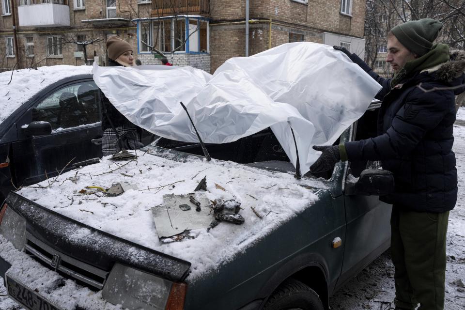 A couple cover their damaged car with a plastic tarp after a Russian attack in Kyiv, Ukraine, Wednesday, Dec. 14, 2022. (AP Photo/Evgeniy Maloletka)