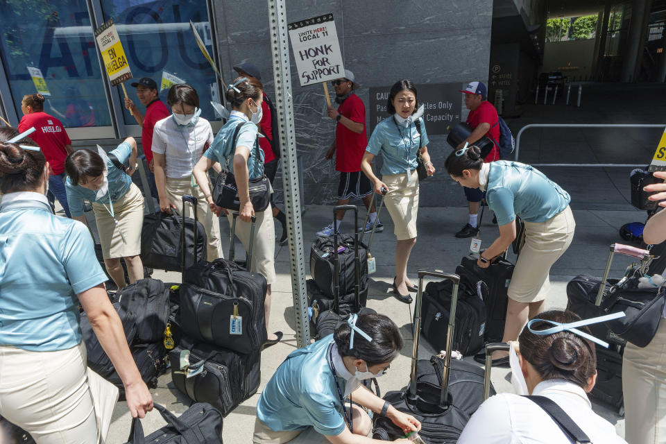 Korean Air Airlines flight attendants get off their bus on the street sidewalk of the InterContinental Los Angeles Downtown as striking hotel workers rally outside Monday, July 3, 2023, in downtown Los Angeles. (AP Photo/Damian Dovarganes)
