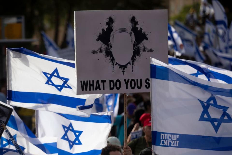 Protestors hold signs and Israeli flags. 