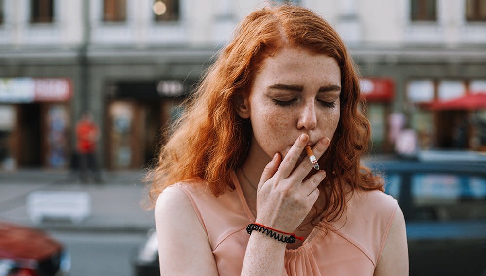 A woman with red hair smoking a cigarette on the street