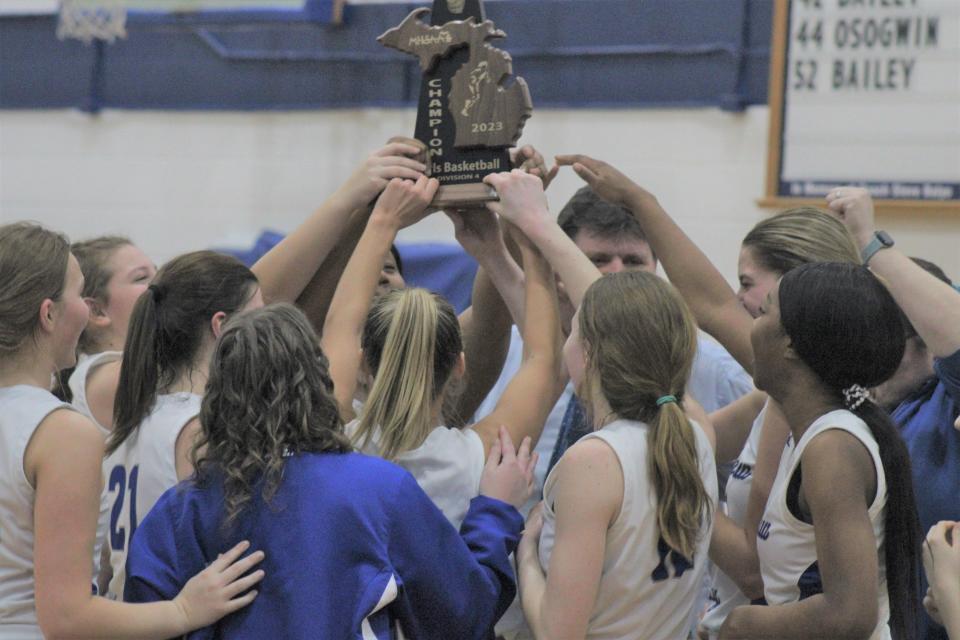 Mackinaw City players and coaches hold up the district title trophy following Friday night's win.