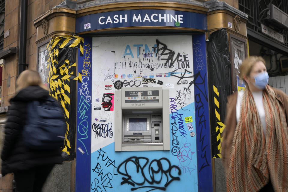 FILE - Shoppers pass a graffitied cash machine in Oxford Street in London, Wednesday, April 13, 2022. Britain’s new Prime Minister Liz Truss has pledged to rebuild the economy, but she faces a daunting job. Truss inherits an ailing economy on the brink of a potentially long recession, with record inflation and millions crying out for government help to cope with energy bills. (AP Photo/Kirsty Wigglesworth, File)