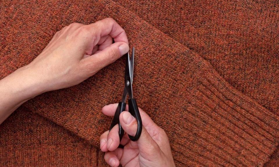 Woman’s hands cutting lint from wool jumper using scissors