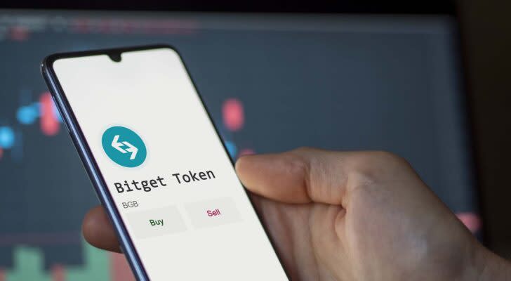 A hand holding a phone showing the Bitget Token logo and name (BGB).