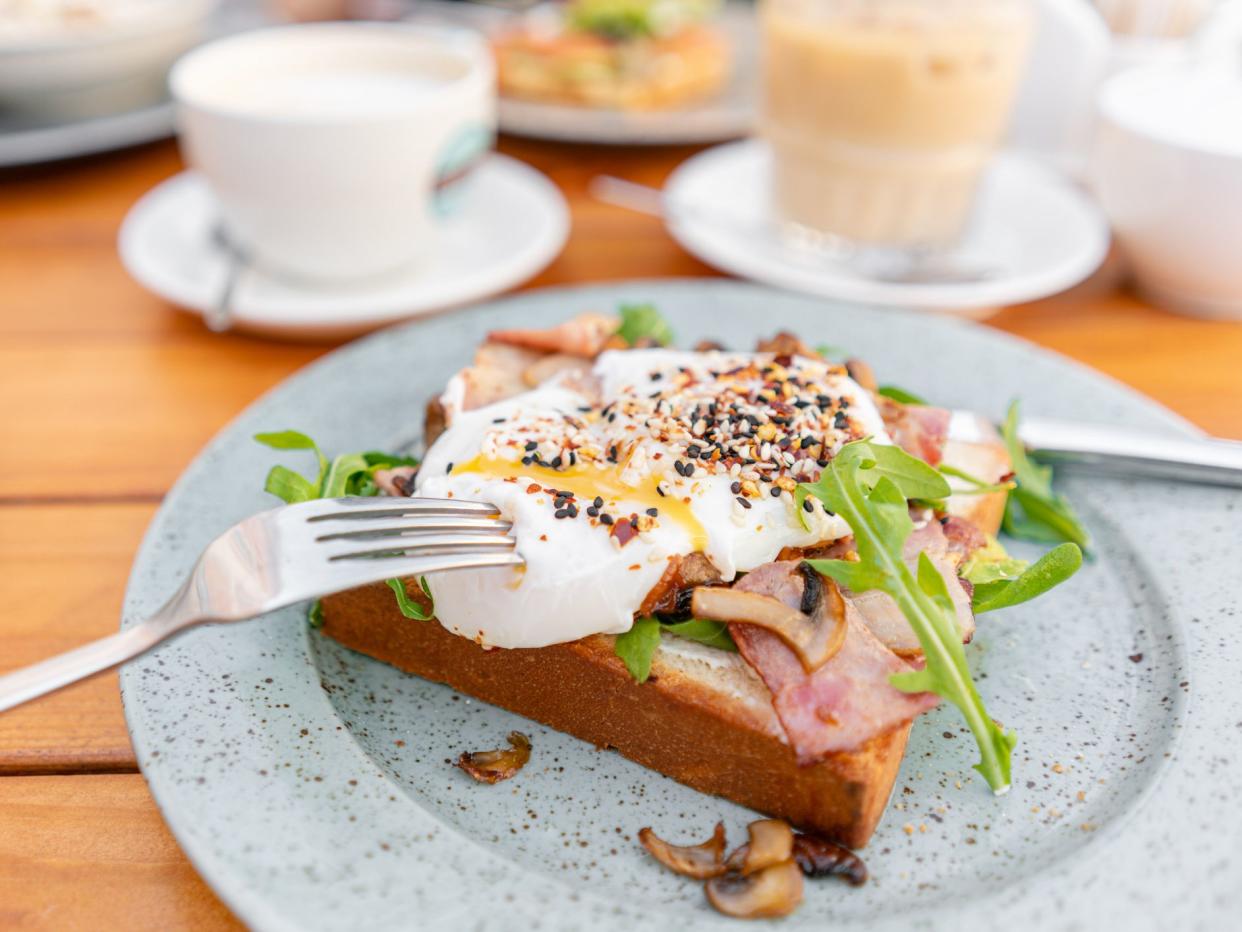 Breakfast and coffee in the summer cafe. Sandwich on a bun brioche with bacon, mushrooms, arugula and poached egg.