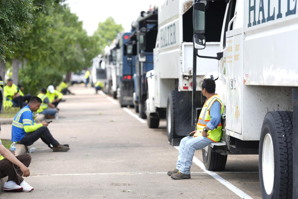 Workers sit along on of several lines of tree trucks from Tennessee and Kentucky stage in a separate lot from the large number of electrical trucks at the AMC Gulf Pointe movie theater at Beltway 8 and I-45 on Saturday, May 18, 2024, in Houston, as help comes in after a strong thunderstorm moved through Thursday evening, knocking out power to nearly a half a million people. (Karen Warren/Houston Chronicle via AP)