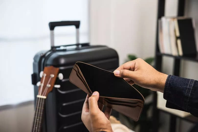 Close up male traveller hand open the empty wallet near trolley bag in the house.There is no money in wallet. No budget to travel