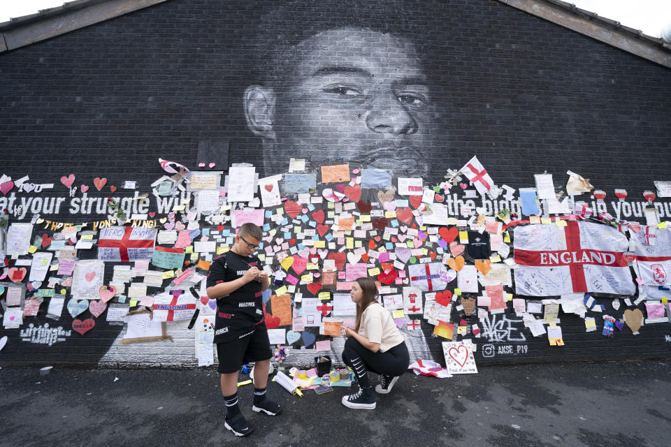 A boy stands by messages of support left on a mural of Manchester United striker and England player Marcus Rashford, on the wall of the Coffee House Cafe on Copson Street, in Withington, Manchester, England, Tuesday July 13, 2021. The mural was defaced with graffiti in the wake of England losing the Euro 2020 soccer championship final match to Italy. (AP Photo/Jon Super)