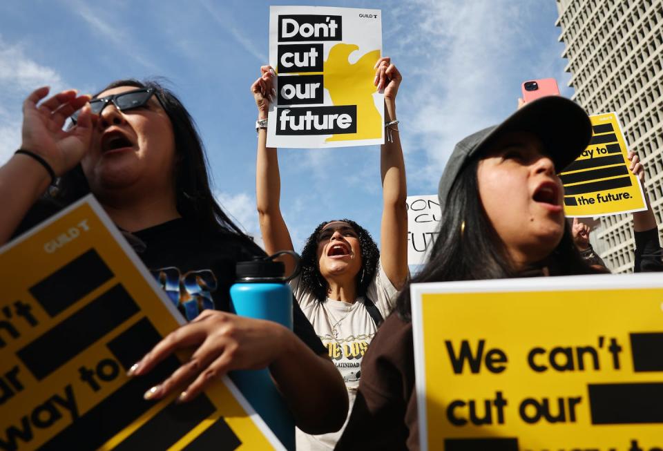 Three female protestors shout, while one holds a sign reading 'Don't cut our future.'