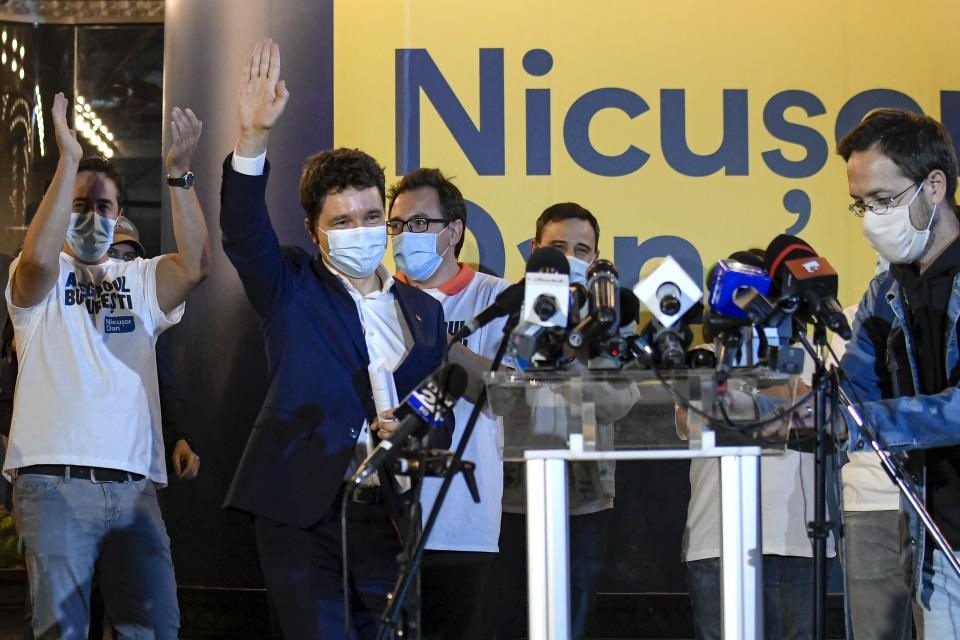 Nicusor Dan, second from right, the mayor candidate backed by the USR-PLUS Alliance and the ruling Liberal Party, wearing a face mask for protection against COVID-19 infection, waves to supporters outside his campaign headquarters in Bucharest, Romania, Sunday, Sept. 27, 2020 after opinion polls indicate he has won the race for the Romanian capital. Dan is placed ahead of the incumbent mayor of the Romanian capital, Gabriela Firea, backed by the Social Democratic Party in local elections. (AP Photo/Andreea Alexandru)