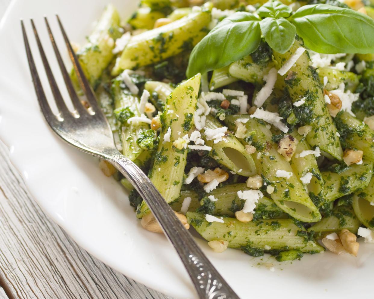 Pesto Penne garnished with fresh basil on a white plate with a fork