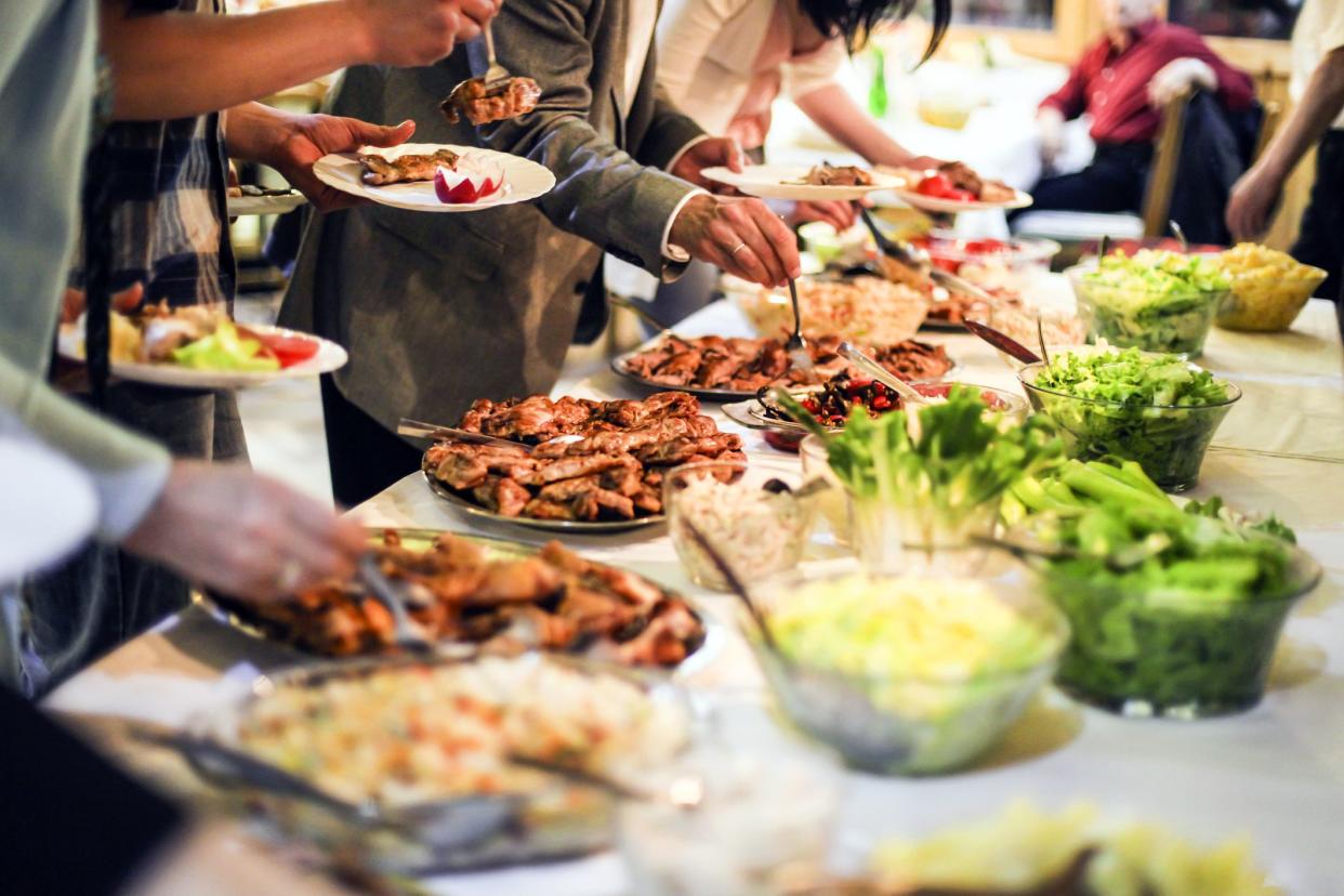 Large group of people picking food (grilled meat and salads) from a buffet table. Unrecognizable Caucasian adults, both female and male.