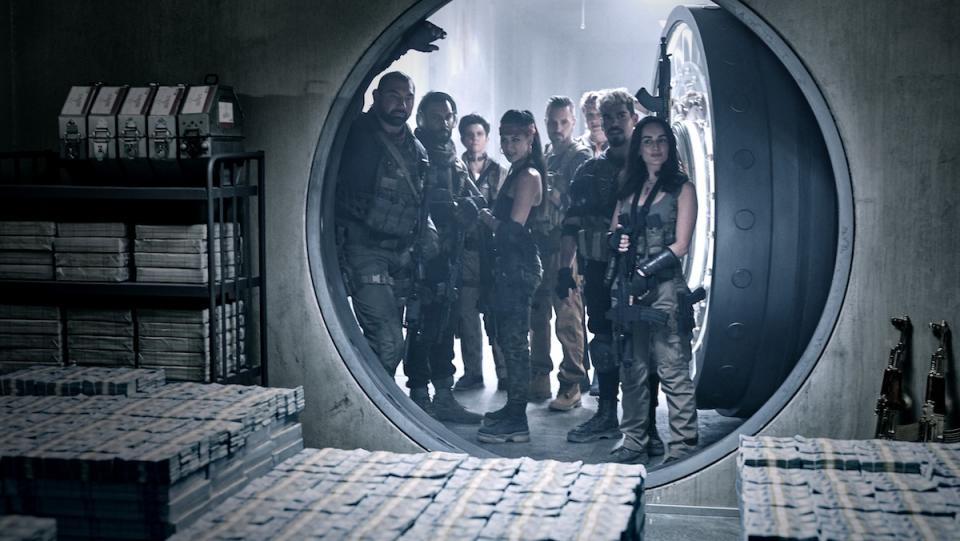 Armed mercenaries in fatigues stand in a round vault door looking at piles of money in Zack Snyder's Army of the Dead