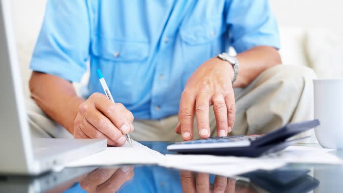 Portrait of a mature man writing something as he uses calculator.