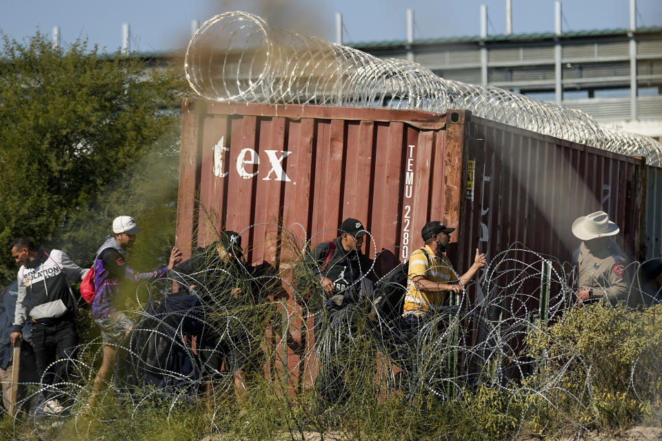 A Texas Department of Public Safety official, right, looks on as migrants walk near a rail car covered in Concertina wire at the Texas-Mexico border, Wednesday, Jan. 3, 2024, in Eagle Pass, Texas. U.S. House Speaker Mike Johnson is leading about 60 fellow Republicans in Congress on a visit to the Mexican border. Their trip comes as they are demanding hard-line immigration policies in exchange for backing President Joe Biden's emergency wartime funding request for Ukraine. (AP Photo/Eric Gay)