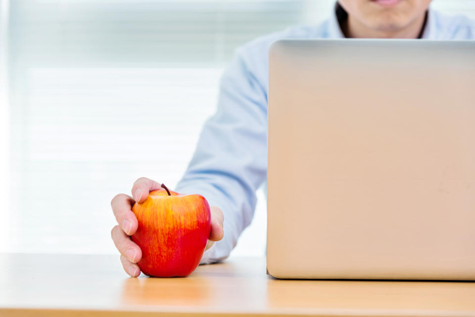 Businessman holding an apple and working on laptop.