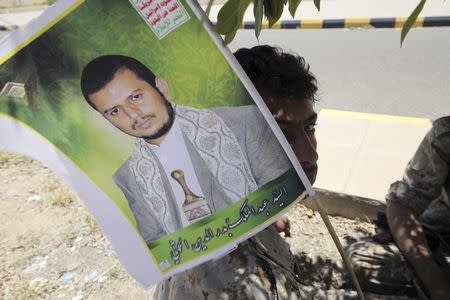 A youth dressed in military uniform holds up a poster of the Houthi movement's leader Abdel-Malek Badruddin al-Houthi as he and a friend sit under a tree after being stationed to provide security during celebrations marking the 25th anniversary of Yemen's unification, in Sanaa May 23, 2015. REUTERS/Mohamed al-Sayaghi