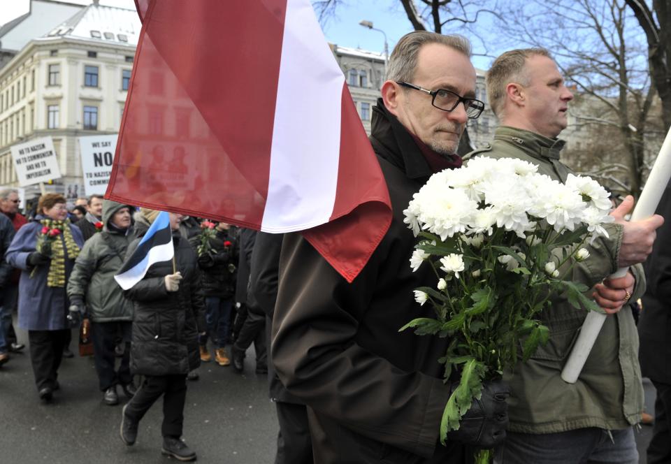 People carry Latvian flags as they march to the Freedom Monument to commemorate World War II veterans who fought in Waffen SS divisions, in Riga, Latvia, Sunday, March 16, 2014. People participate in annual commemorations of Latvian soldiers who fought in Nazi units during WWII. a woman at the background holds Estonian flag. (AP Photo/Roman Kosarov, F64 Photo Agency)