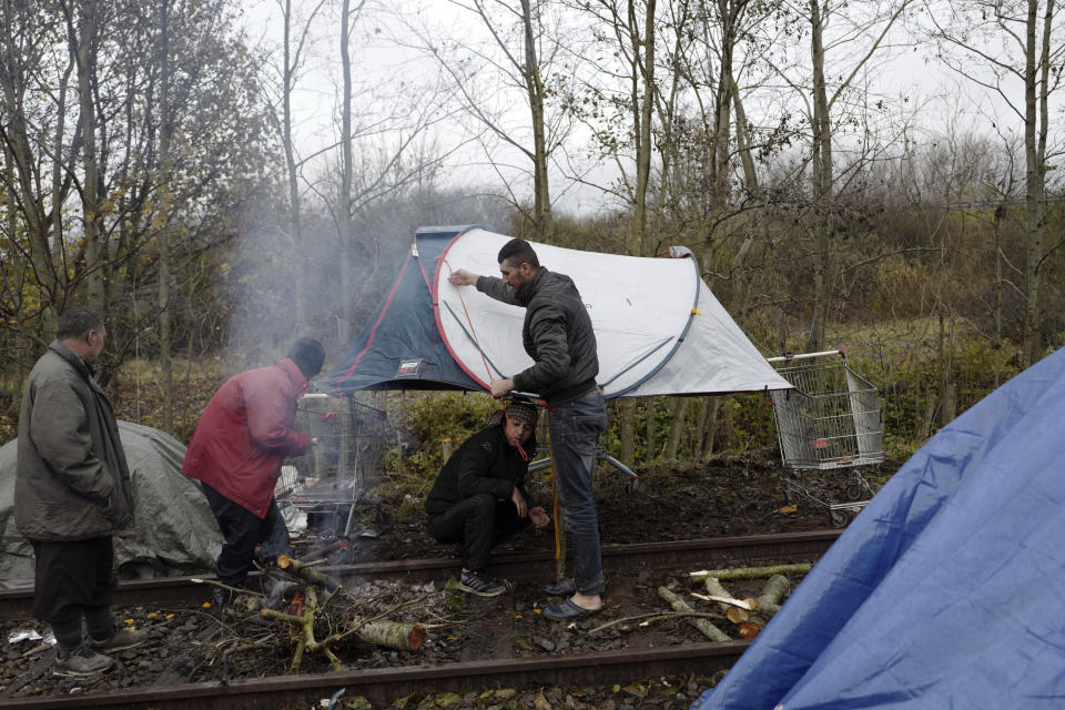 Migrants protect their fire from the rain with a tent in a makeshift camp outside Calais, northern France, Saturday, Nov. 27, 2021. At the makeshift camps outside Calais, migrants are digging in, waiting for the chance to make a dash across the English Channel despite the news that at least 27 people died this week when their boat sank a few miles from the French coast. (AP Photo/Rafael Yaghobzadeh)