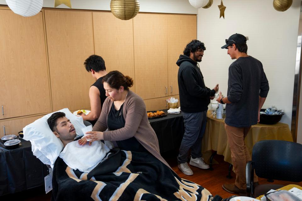 Jonathan Avalos watches the Purdue Boilermakers play NC State in the NCAA Men’s Basketball Tournament Final Four game with his sister, cousin and best friends, while Maria Avalos, his mother, helps him take a drink, Saturday, April 6, 2024, in the B5 Comfort Care unit at the IU Health Methodist Hospital in Indianapolis. Jonathan Avalos is a 22-year-old Purdue student with glioblastoma, an incurable type of primary brain cancer. St. Elmo Steak House catered Jonathan’s favorite meal: steak and crab legs.