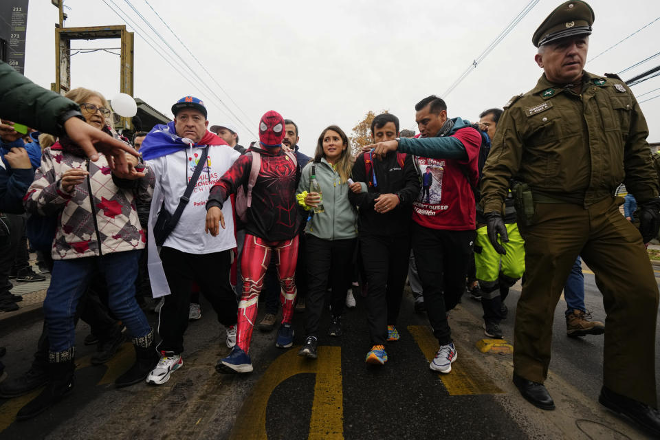 Camila Gómez, madre de Tomás Ross, de 5 años, que padece distrofia muscular de Duchenne, en el centro, está acompañada por simpatizantes cuando llega a pie a Santiago, Chile, después de caminar durante aproximadamente un mes para recaudar fondos para el tratamiento médico de su hijo la madrugada del miércoles 29 de mayo de 2024. (AP Foto/Esteban Félix)