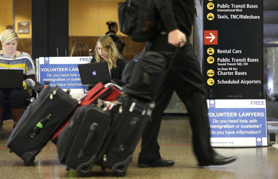 Asti Gallina, center, a volunteer law student from the University of Washington, works at a station near where passengers arrive on international flights at Seattle-Tacoma International Airport Tuesday, Feb. 28, 2017, in Seattle. Gallina was volunteering with the group Airport Lawyer, which also offers a secure website and mobile phone app that alerts volunteer lawyers to ensure travelers make it through customs without trouble. Airport officials and civil rights lawyers around the country are getting ready for President Donald Trump's new travel ban, which is expected to be released as soon as Wednesday. (AP Photo/Ted S. Warren)