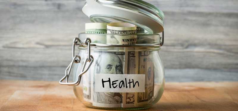 A glass money jar labeled health that's full of cash.