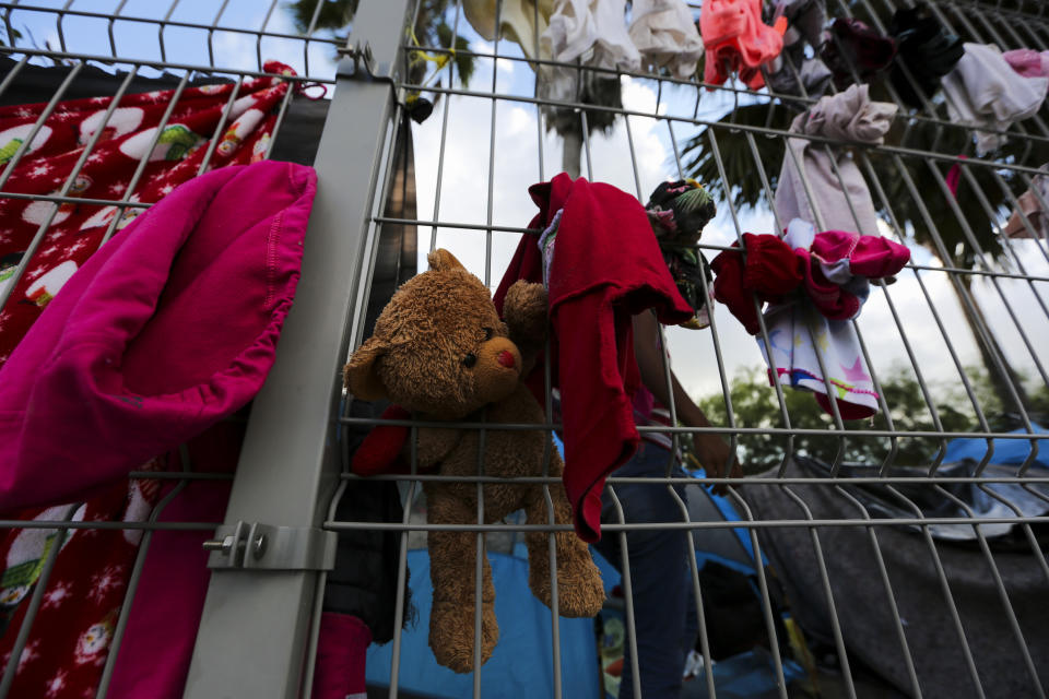 In this Oct. 11, 2019 photo, a stuffed teddy bear hangs in a fence amid clothing at a migrant camp set up near a legal port of entry bridge that connects Matamoros, Mexico with Brownsville, Texas. There’s not enough space for everyone at the shelters, so many rent rooms, ranging from $35 per person per month for a spot in a cramped five-person bedroom in a seedy area, to $300-$500 for a more secure home. But nowhere is truly safe. (AP Photo/Fernando Llano)