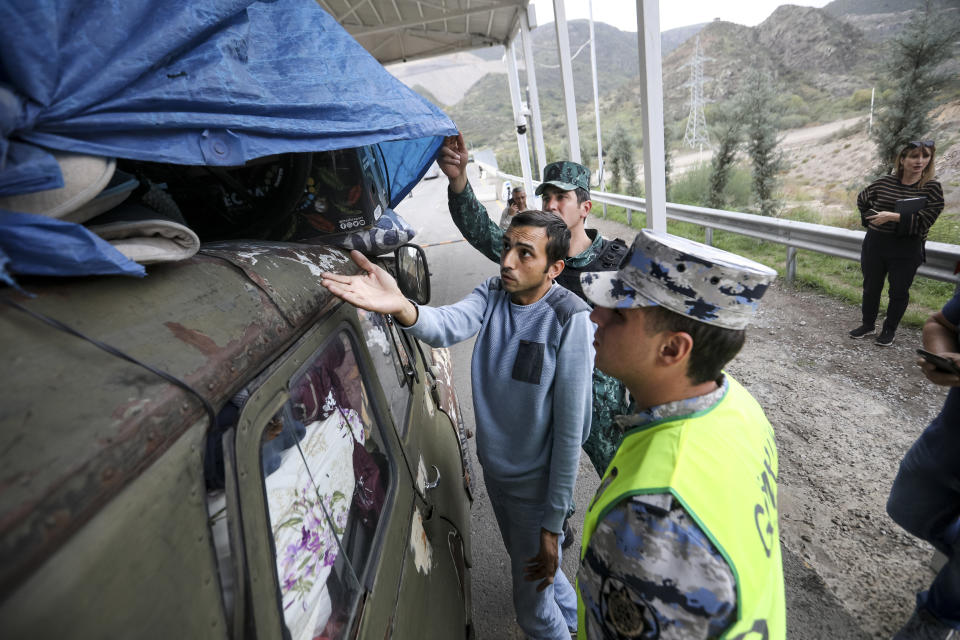 Sergey Astsetryan, an ethnic Armenian resident of Nagorno-Karabakh, center, shows his belongings as Azerbaijani border guard servicemen check his Soviet-made vehicle at the Lachin checkpoint on the way from Nagorno-Karabakh to Armenia, in Azerbaijan, Sunday, Oct. 1, 2023. Astsetrayn was one of the last residents of Nagorno-Karabakh to drive out of the region in his own vehicle as part of a grueling weeklong exodus of over 100,000 people — more than 80% of the residents — after Azerbaijan reclaimed the area in a lightning military operation. (AP Photo/Aziz Karimov)