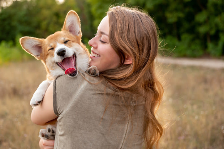 A woman holding a corgi in a field