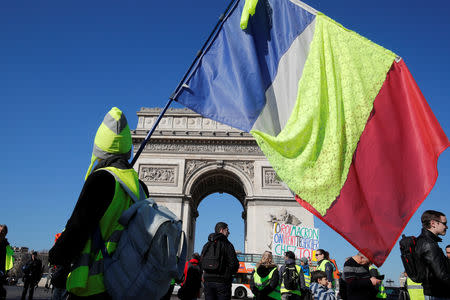 A French flag with a yellow band is held by a protester wearing a yellow vest on the Champs Elysees near the Arc de Triomphe during a demonstration by the "yellow vests" movement in Paris, France, February 23, 2019. REUTERS/Philippe Wojazer