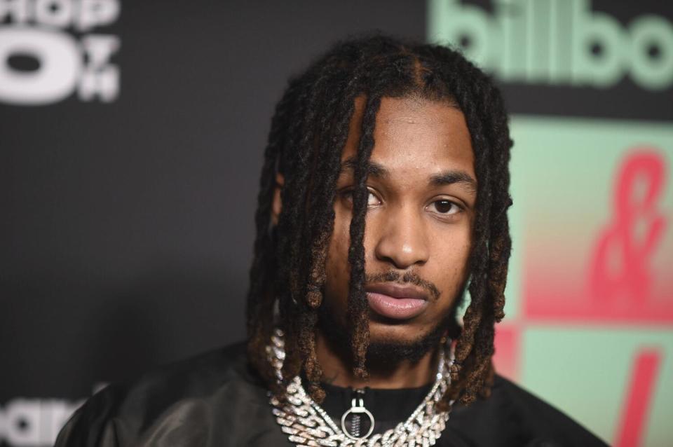 A young man with braids wears thick silver chains and looks straight ahead