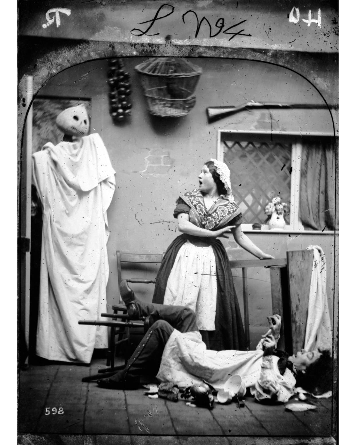 A white caped figure wearing a haloween pumpkin mask taking two people by surprise in their kitchen.