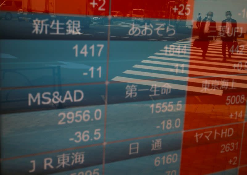 Passersby wearing protective face masks are reflected on a stock quotation board outside a brokerage, amid the coronavirus disease (COVID-19) outbreak, in Tokyo