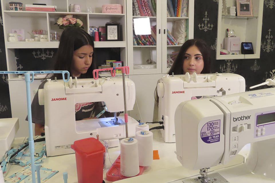 Giuliana Demma, left, and her sister Audrina, right, sew pediatric hospital gowns in the basement of her Freehold, N.J., home on June 19, 2024. The sisters have sewn and donated 1,800 hospital gowns to sick children in 36 states plus Africa. Giuliana was inspired by seeing her baby cousin wearing an ugly, ill-fitting gown while hospitalized with brain cancer in 2017. (AP Photo/Wayne Parry)