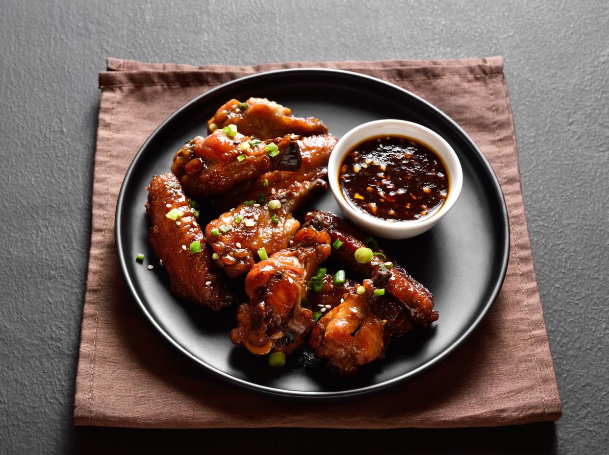 Sticky honey-soy chicken wings on plate over dark stone background. Close up view
