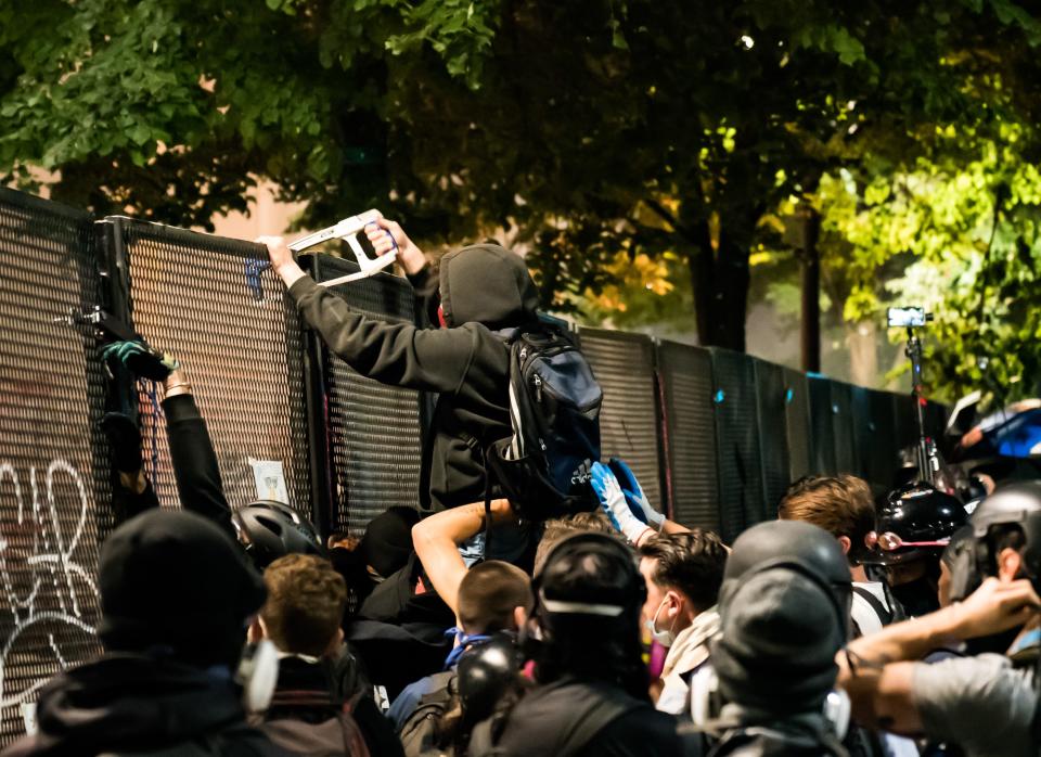 A person tries to cut through a metal bolt holding together a portion of the security fence ringing the federal courthouse in Portland, Oregon, in the early hours of July 24, 2020.