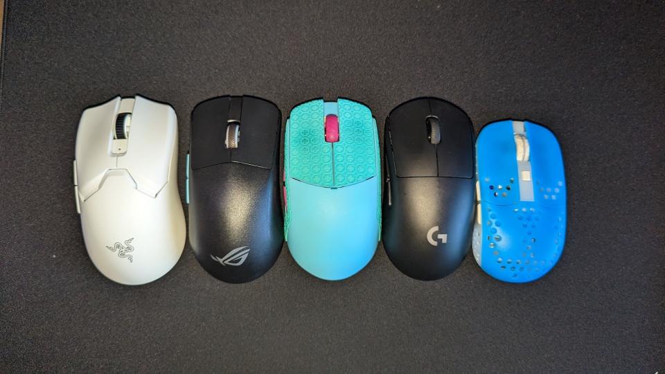 Five mice of different brands and colours on a mousepad for shape somparison.