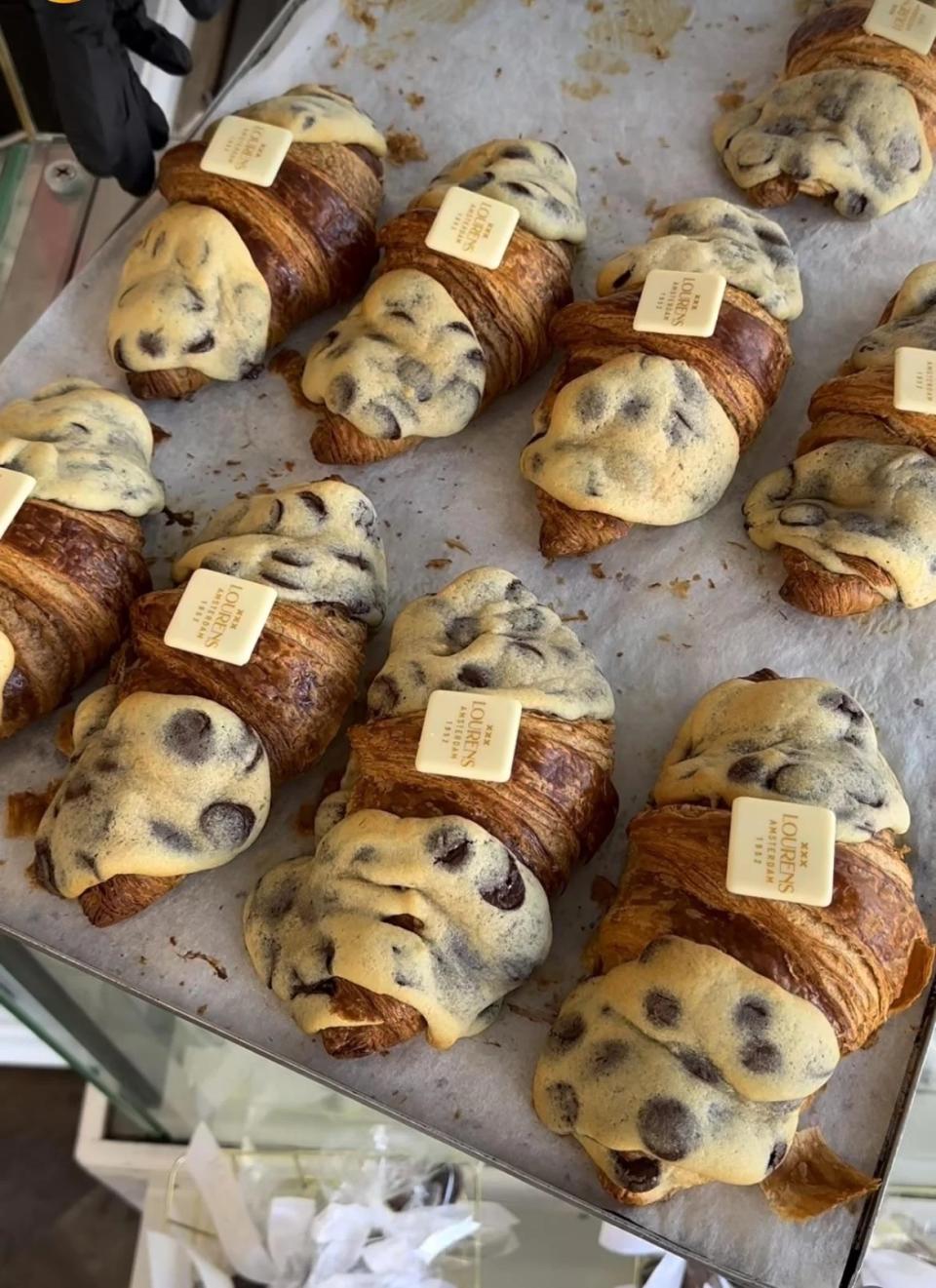 Various croissants with toppings on a tray in a bakery display.  Some have a chocolate chip coating