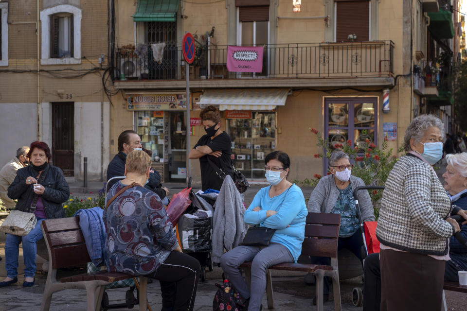 People wearing face masks to protect from coronavirus, sit in a square in Barcelona, Spain, Friday, Oct. 23, 2020. Spain has reported 1 million confirmed infections — the highest number in Western Europe — and at least 34,000 deaths from COVID-19, although experts say the number is much higher since many cases were missed because of testing shortages and other problems. (AP Photo/Emilio Morenatti)