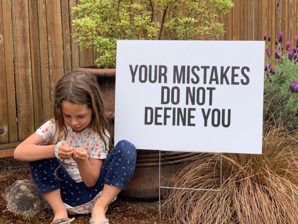 The Seattle father's daughter, Caelyn, is seen here sitting next to another sign, reading: 'Your mistakes do not define you'.