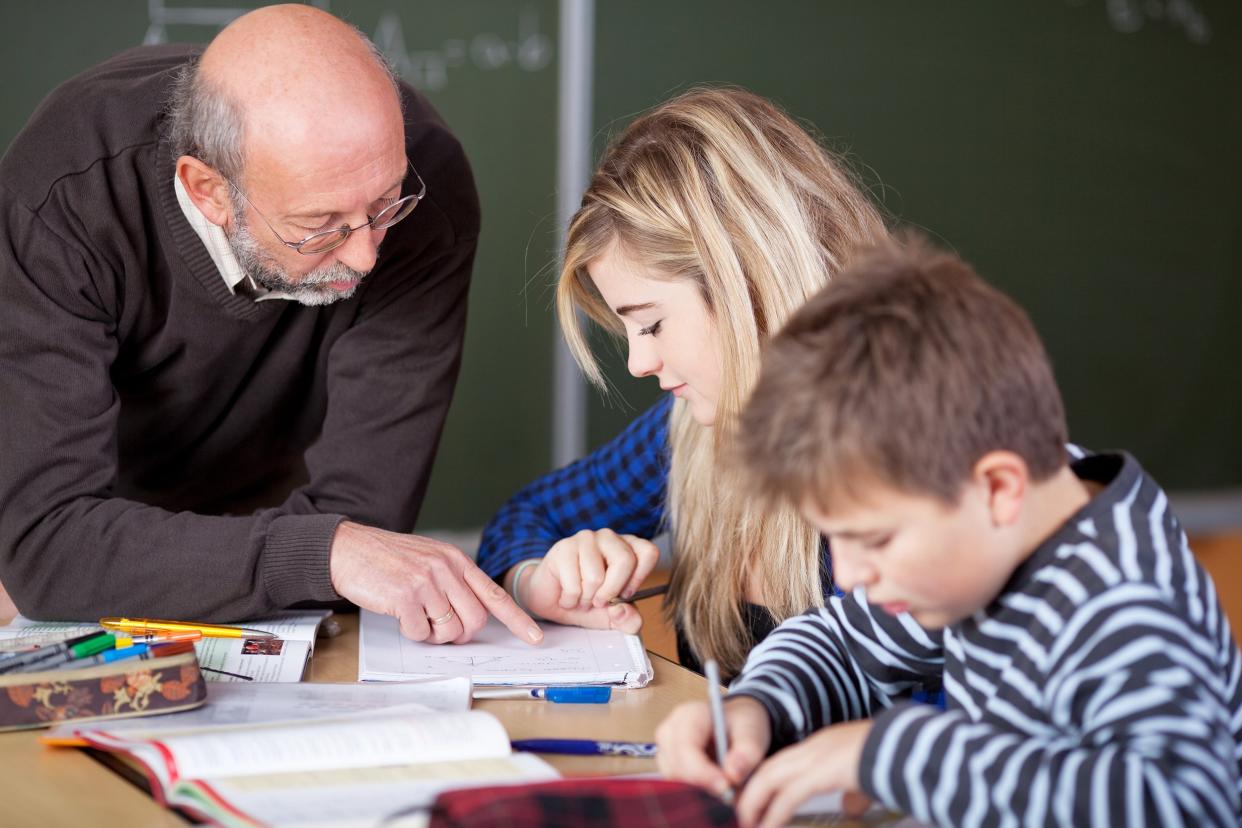 senior male teacher teaching student at desk in classroom