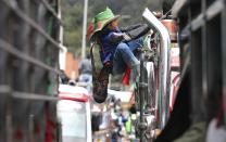 An Indigenous youth climbs the side of a bus during a national strike in Bogota, Colombia, Wednesday, Oct. 21, 2020. Workers' unions, university students, human rights defenders, and Indigenous communities held a day of protest in conjunction with a national strike across Colombia to protest against the assassinations of social leaders, in defense of the right to protest and to demand advances in health, income and employment. (AP Photo/Fernando Vergara)