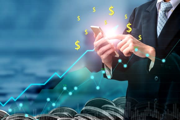 Businessman holding cell phone with line chart going up and dollar signs in foreground