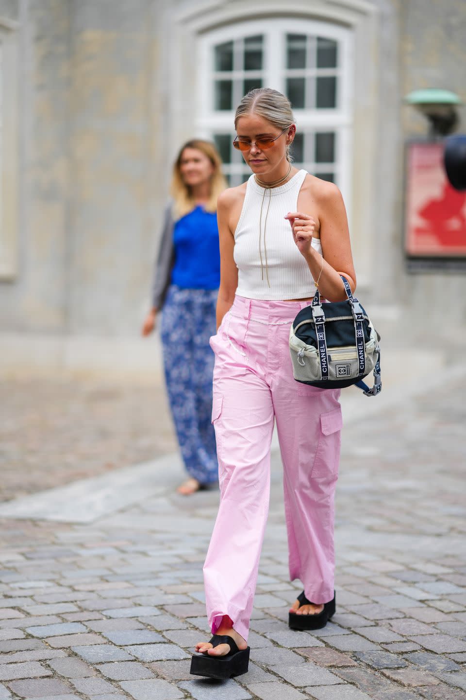 copenhagen, denmark august 09 a guest wears orange sunglasses, gold and diamonds earrings, a brown suede necklace, a white ribbed halter neck cropped tank top, pale pink large cargo pants, a beige and black fabric handbag from chanel, black platform flip flop, outside aeron, during copenhagen fashion week springsummer 2023, on august 09, 2022 in copenhagen, denmark photo by edward berthelotgetty images
