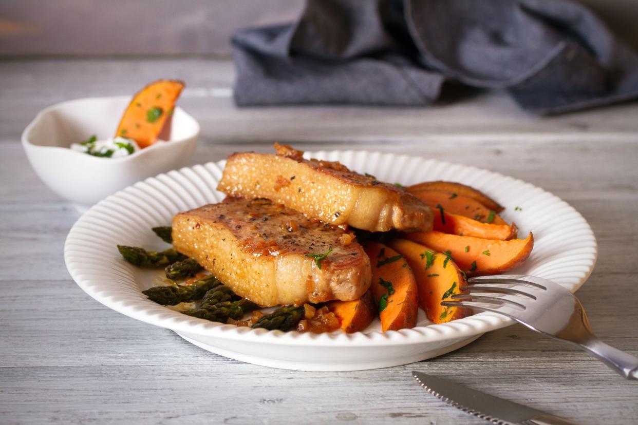 Juicy broiled pork chop steaks with asparagus, sweet potatoes and yogurt sauce.  horizontal image