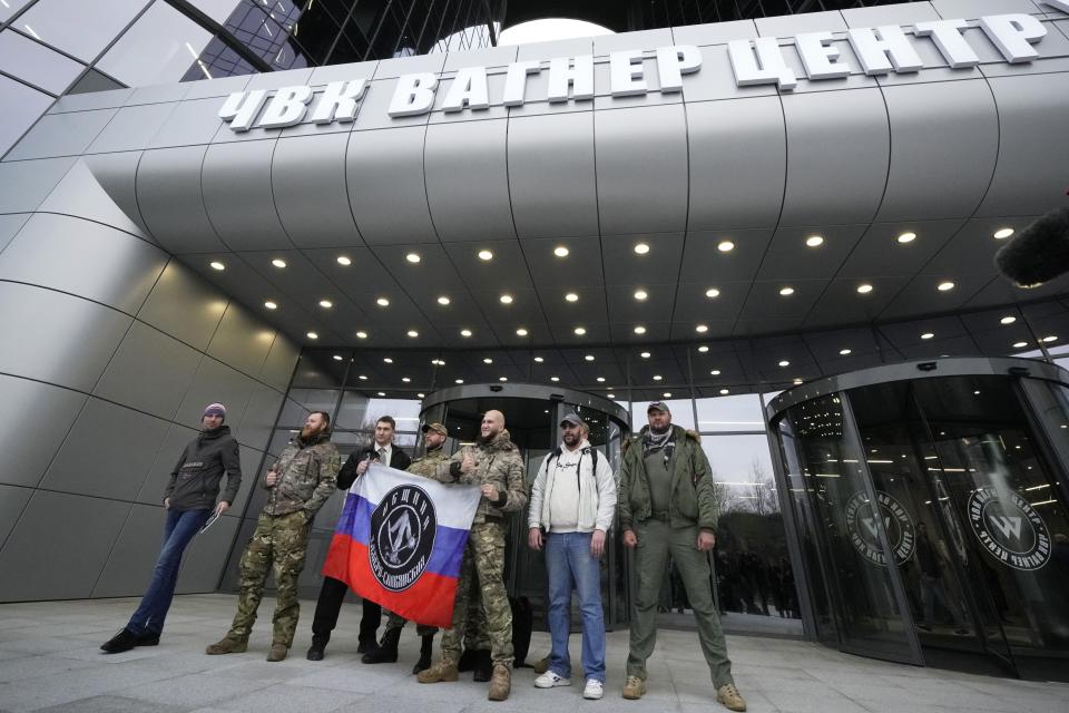 FILE - Visitors wearing military camouflage pose at the entrance of the 'PMC Wagner Centre', which is associated with businessman and founder of the Wagner private military group Yevgeny Prigozhin, during the official opening of the office block during National Unity Day, in St. Petersburg, Russia, Friday, Nov. 4, 2022. The 61-year-old Prigozhin, who has expanded his assets from catering business to Wagner and then mining and other spheres, has scathingly criticized the top military brass for their blunders in Ukraine, charging that Wagner was much more efficient than regular troops. (AP Photo, File)