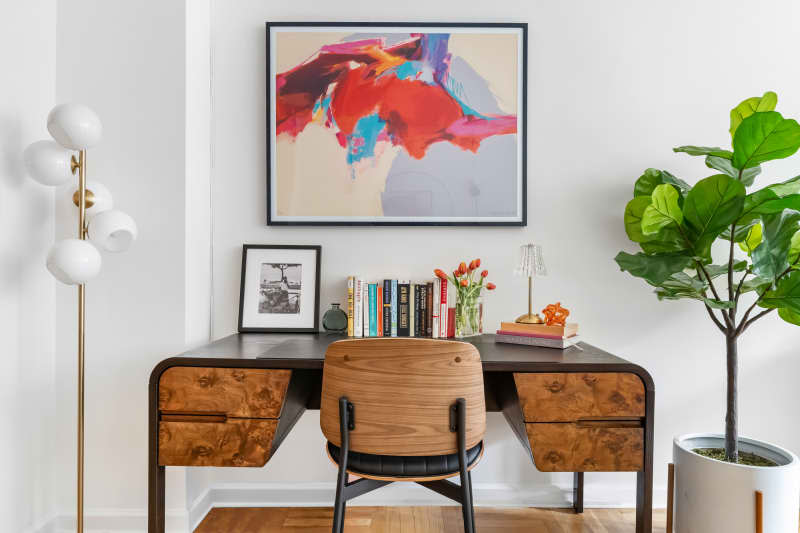 White workspace area with wood desk and chair, books, and statement art